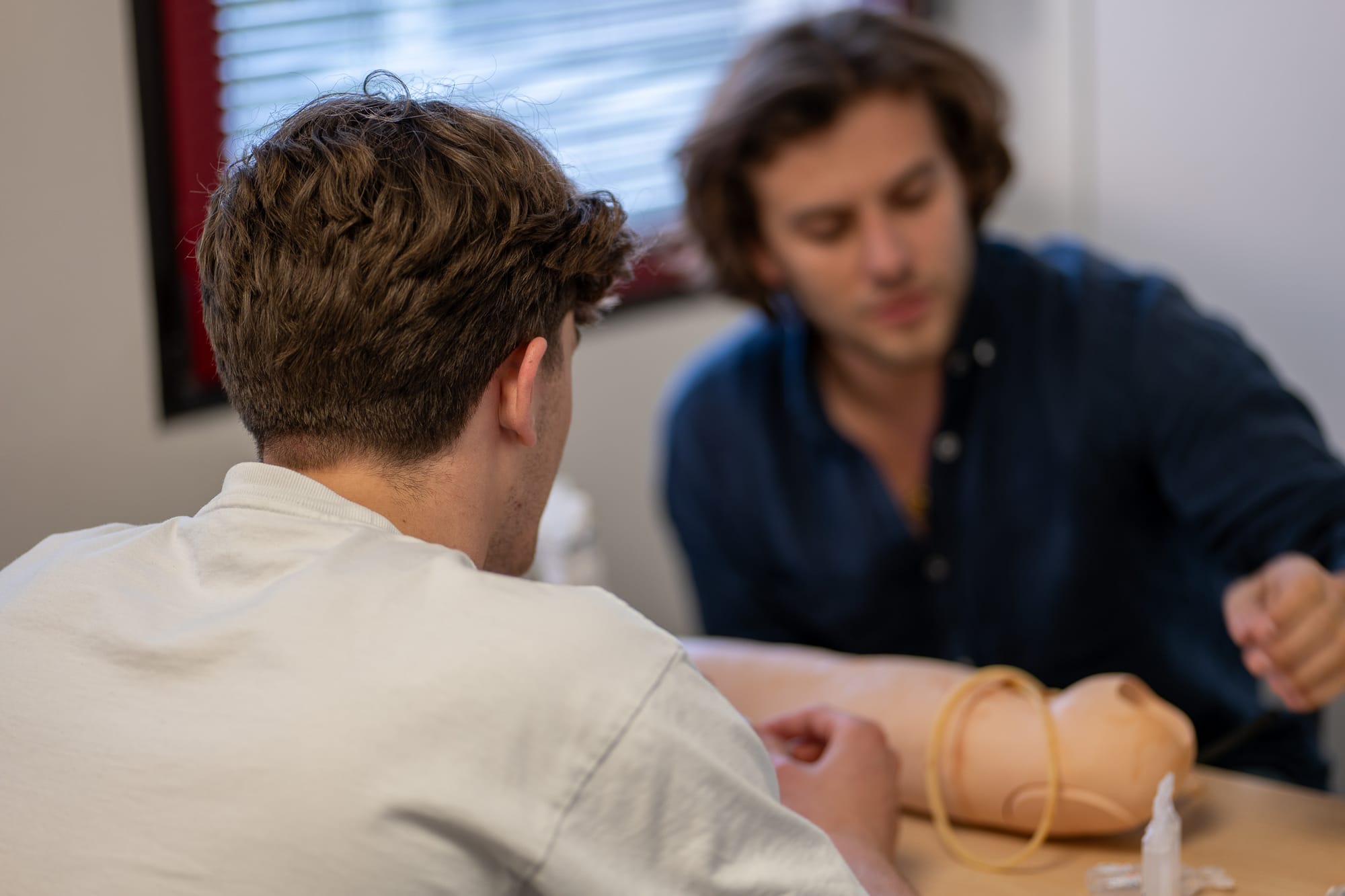 Deux étudiants s'entraînent sur un bras de mannequin dédié à la prise de sang.
